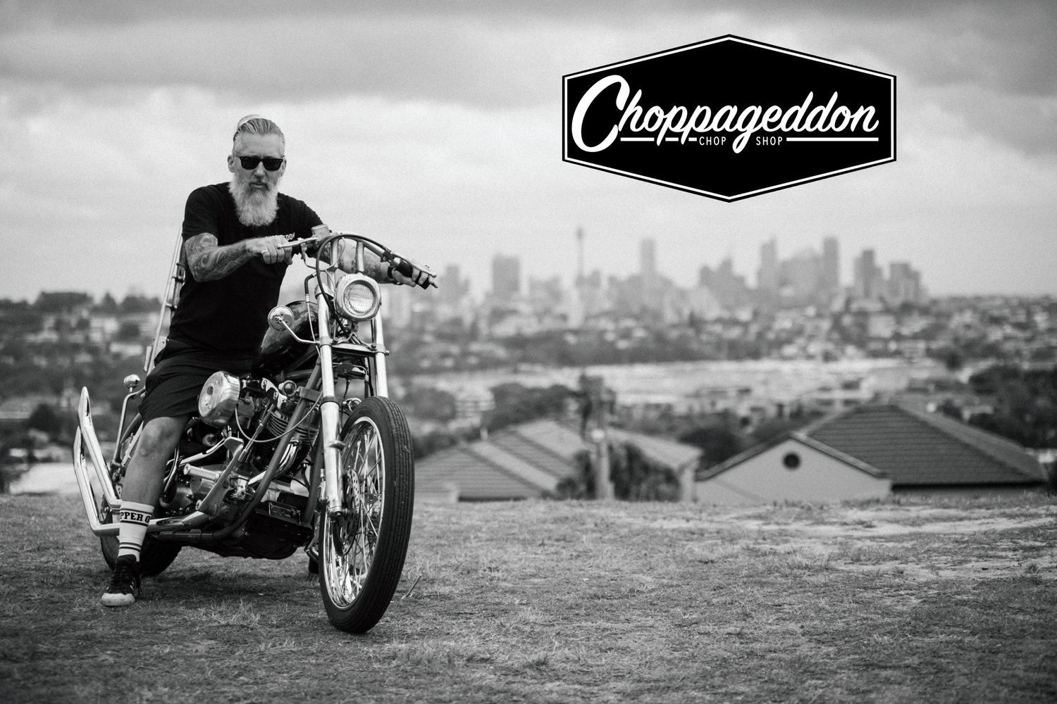 Man posing on a custom chopper motorcycle with a city skyline in the background.