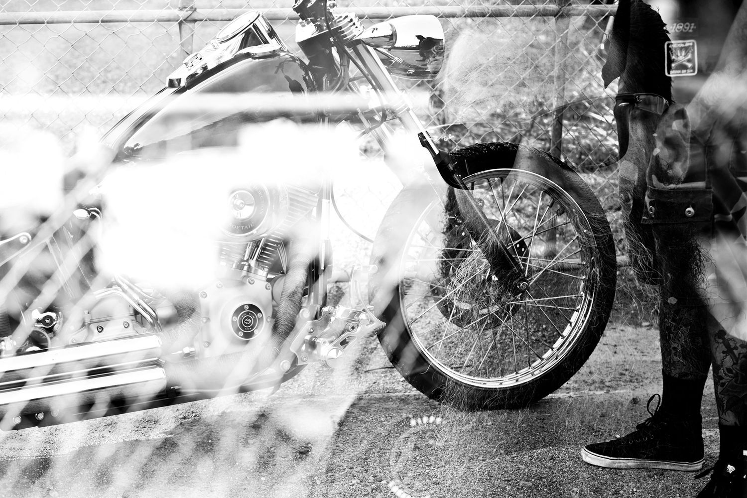 Black and white double exposure photo of a motorcycle wheel and person standing on a city street.