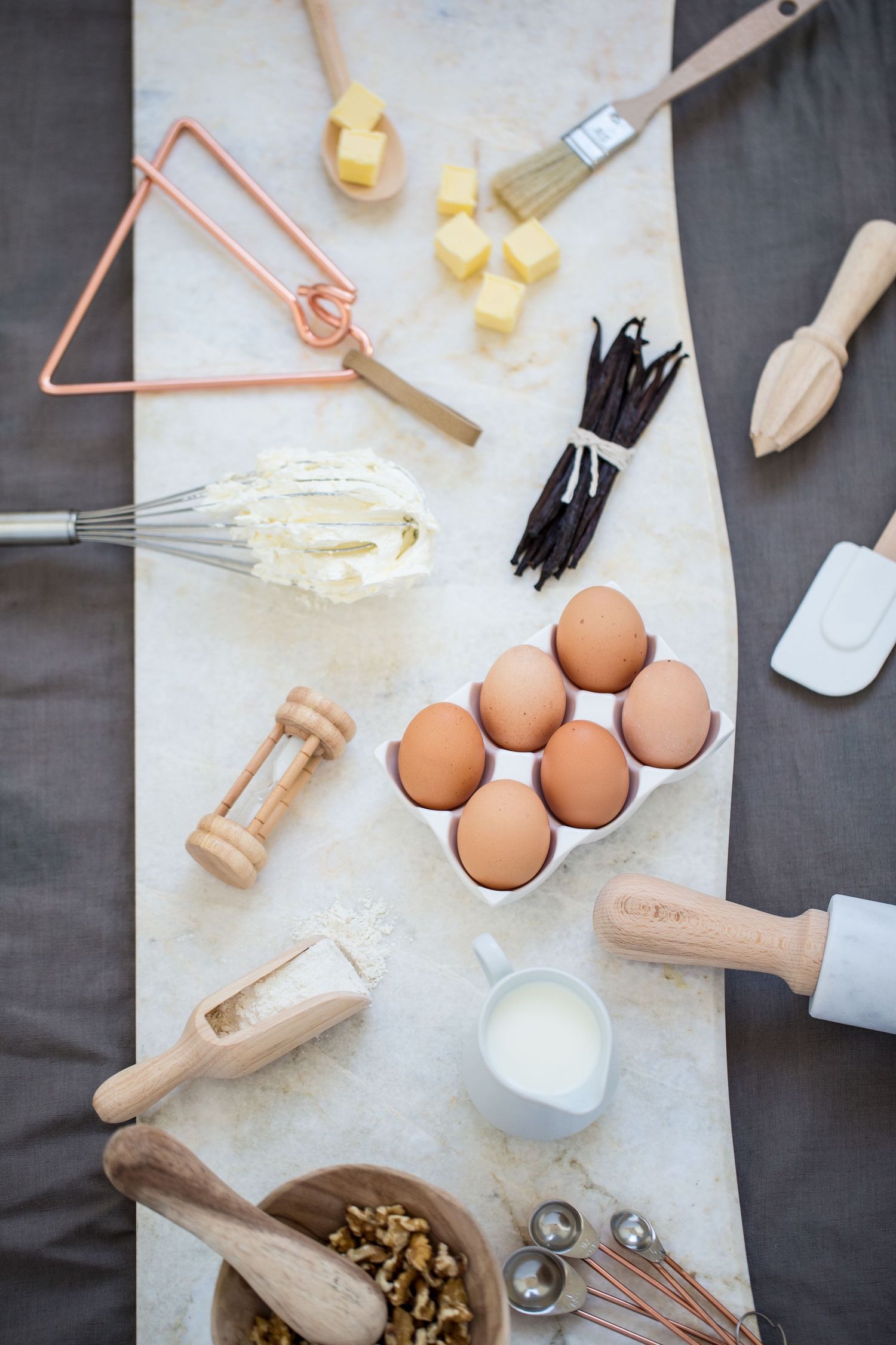 Flat lay of baking ingredients including eggs, butter, vanilla beans, milk, and kitchen tools.