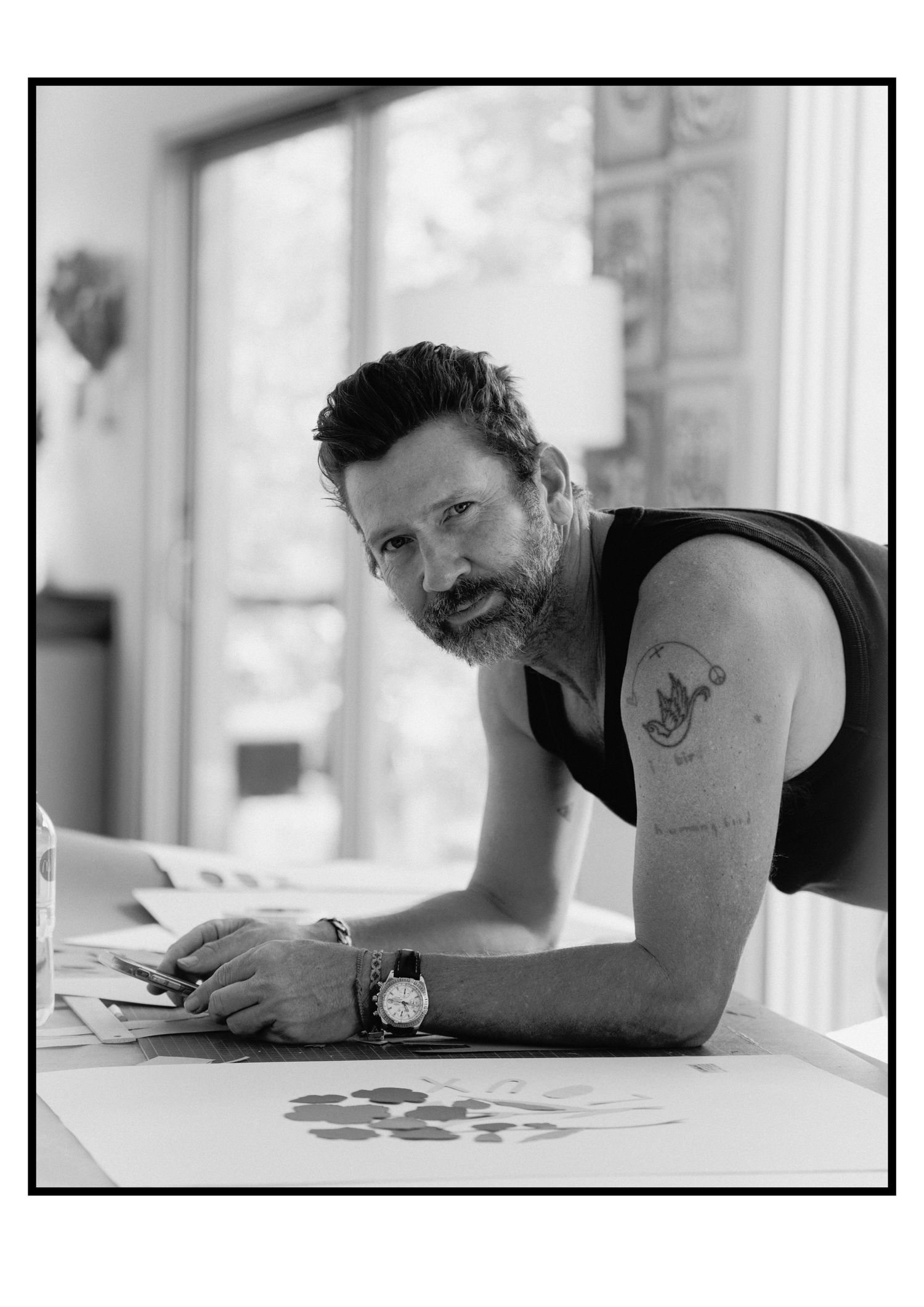 Bearded male artist with tattoo leaning on desk, black and white portrait photo.