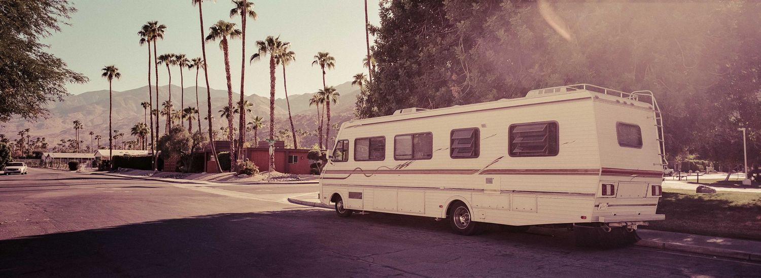 A large white RV parked on a sunny palm tree-lined street in Palm Springs California.