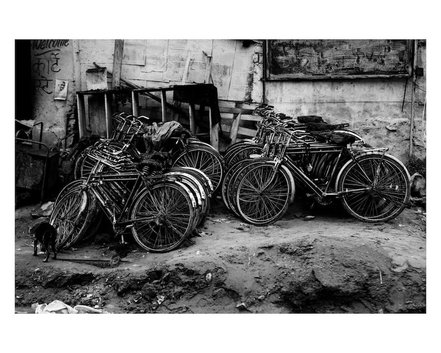 Black and white photograph of abandoned old bicycles leaning against a crumbling urban wall.