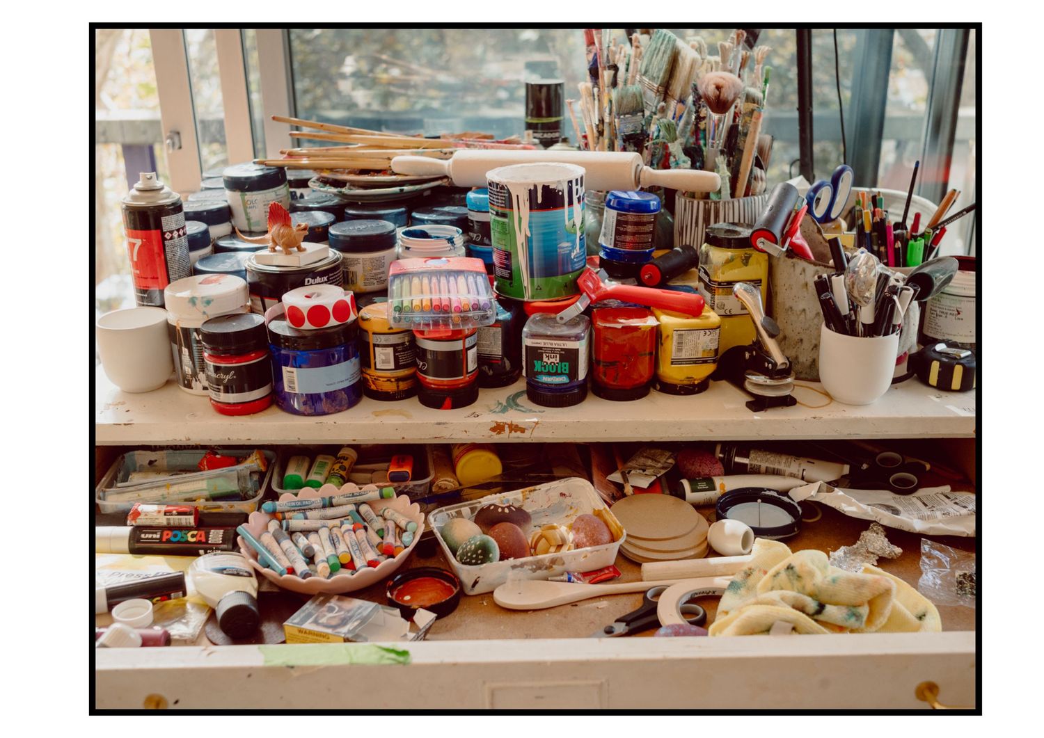 Colorful artist studio workspace with paint jars, brushes, and art supplies on shelves.