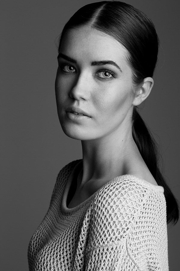 Black and white close-up portrait of a young woman with sleek pulled-back hair wearing a mesh sweater.