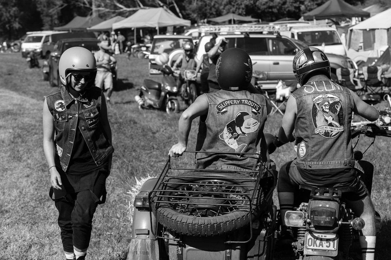 Black and white photo of motorcyclists in vests at an outdoor biker rally event.