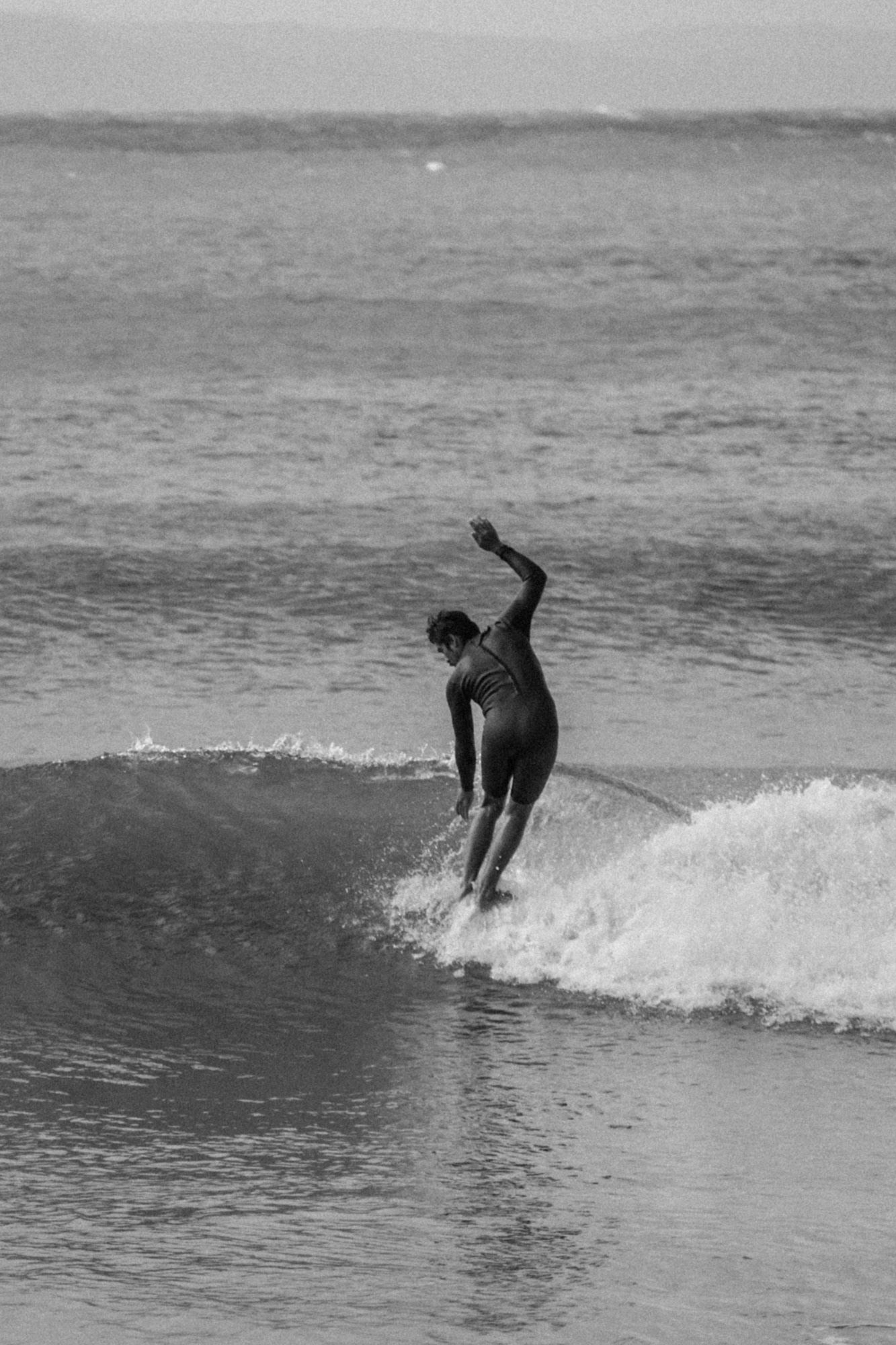 Black and white photo of a surfer riding a wave with one arm raised in the ocean.