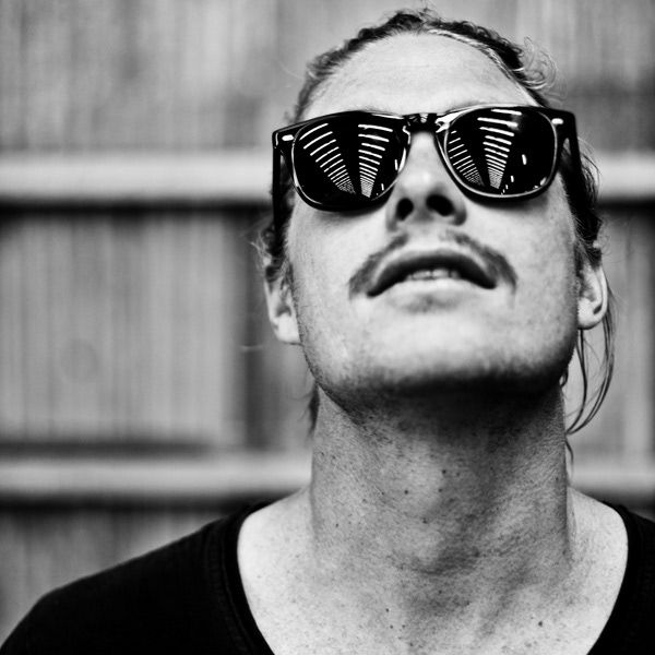 Black and white portrait of a man with sunglasses and mustache looking upward.