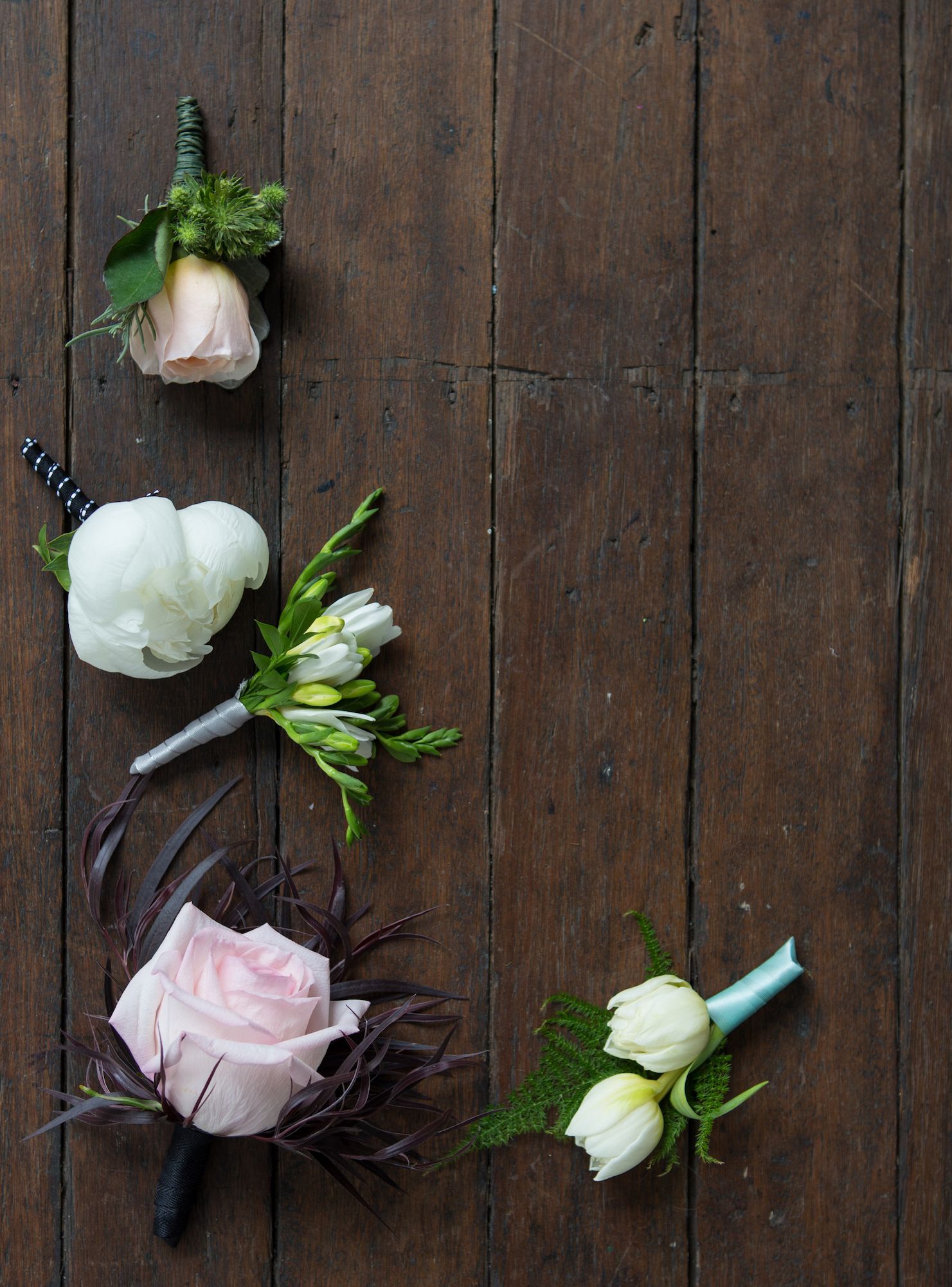 Five elegant wedding boutonnieres with white and pink roses on rustic dark wood.