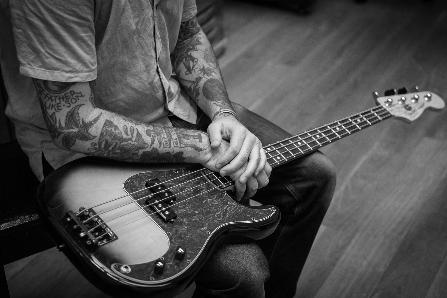 Tattooed musician playing a vintage sunburst bass guitar in black and white photography.