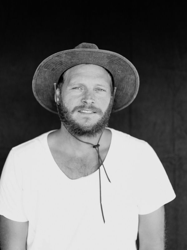 Black and white portrait of a bearded man wearing a wide-brim hat and white t-shirt.
