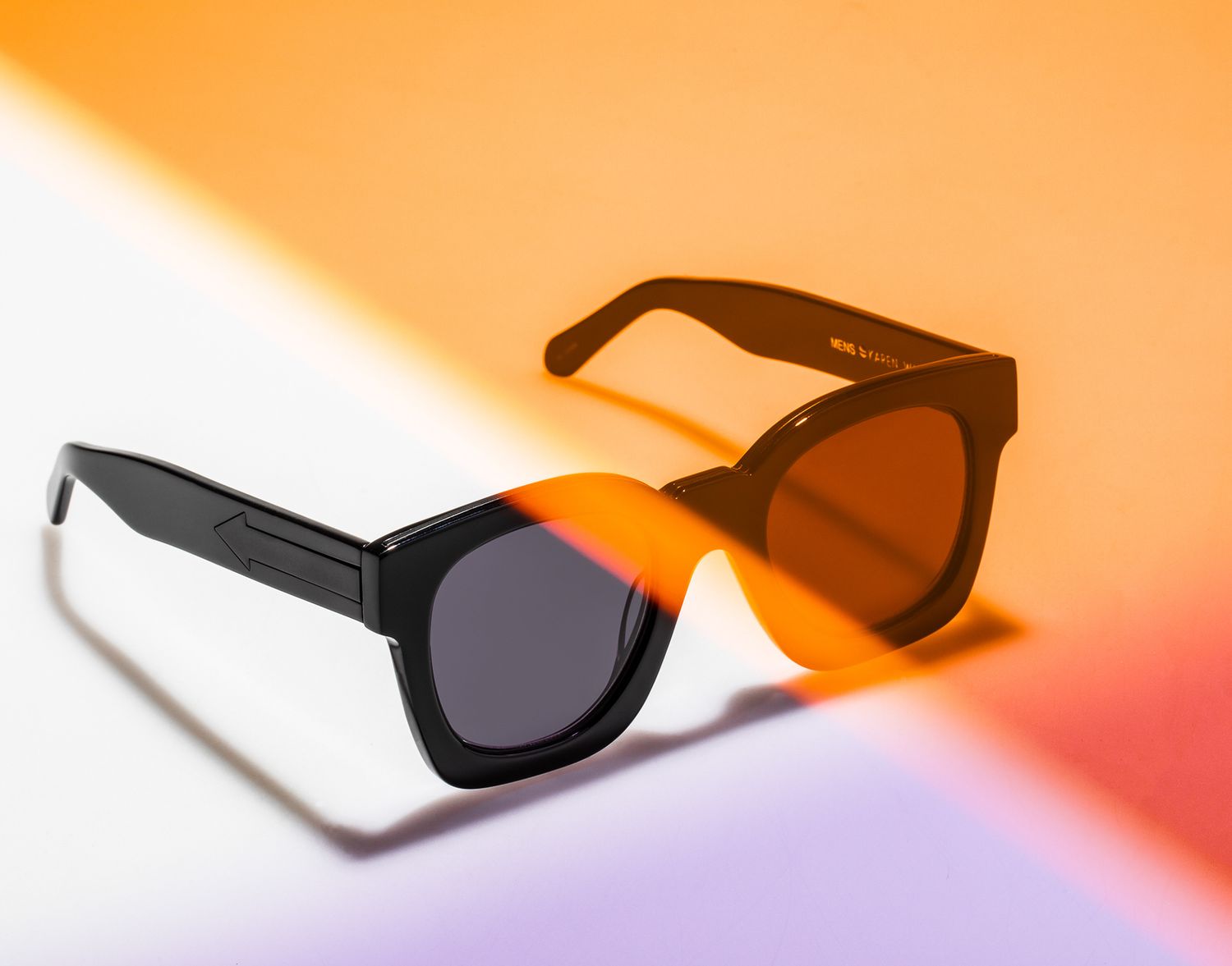 Stylish black oversized sunglasses with dark lenses on colorful orange and white background.