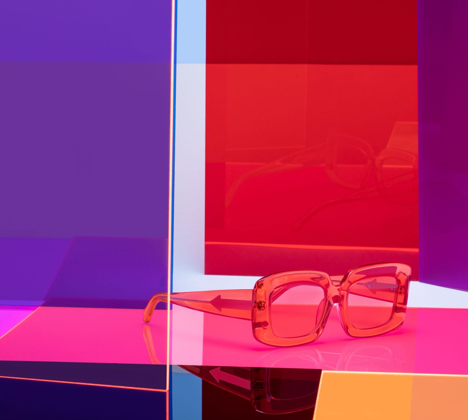 Vibrant pink square sunglasses displayed against colorful red, purple, and pink geometric panels.