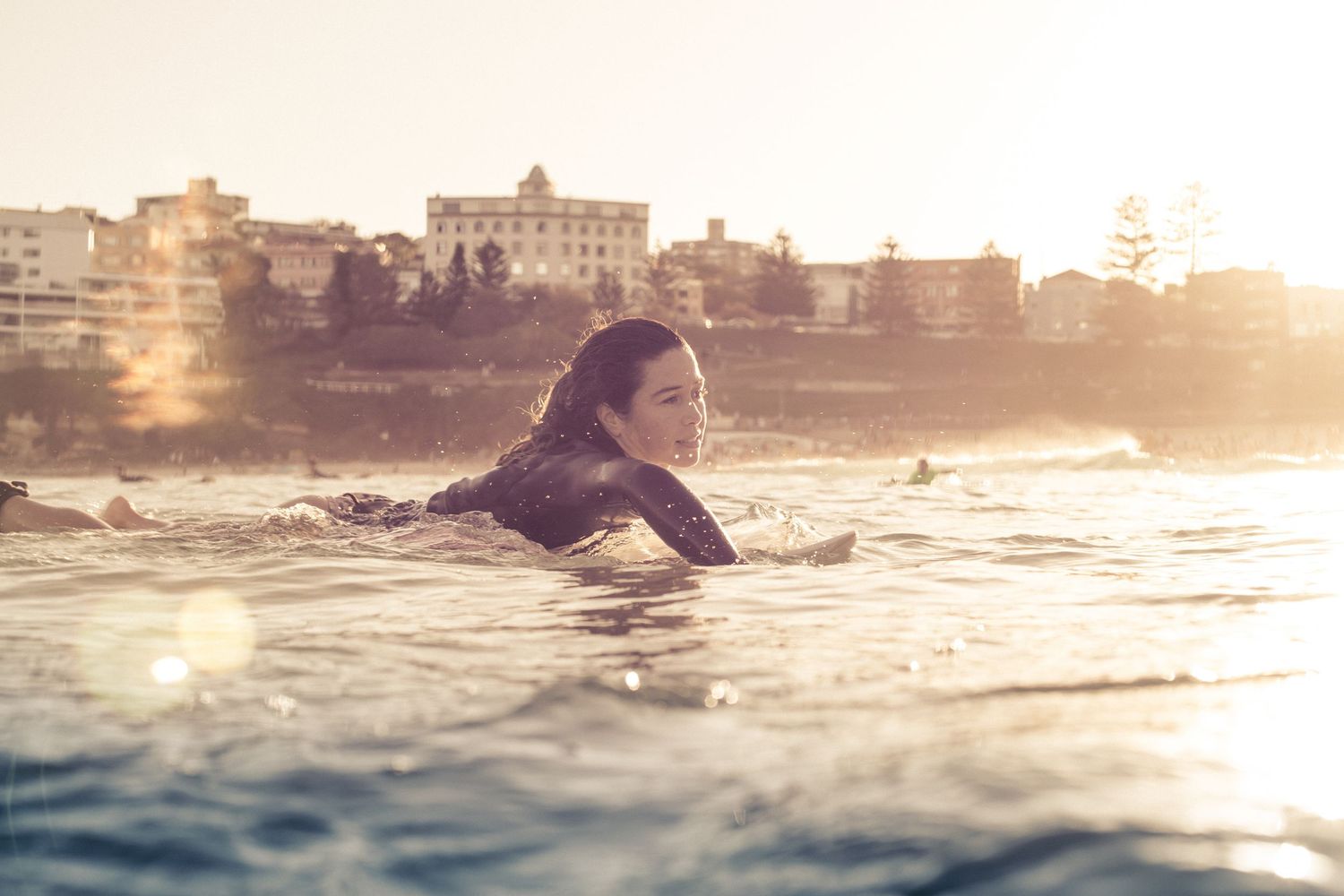 Woman in wetsuit lying on surfboard in golden sunset light at Bondi Beach Sydney Australia.