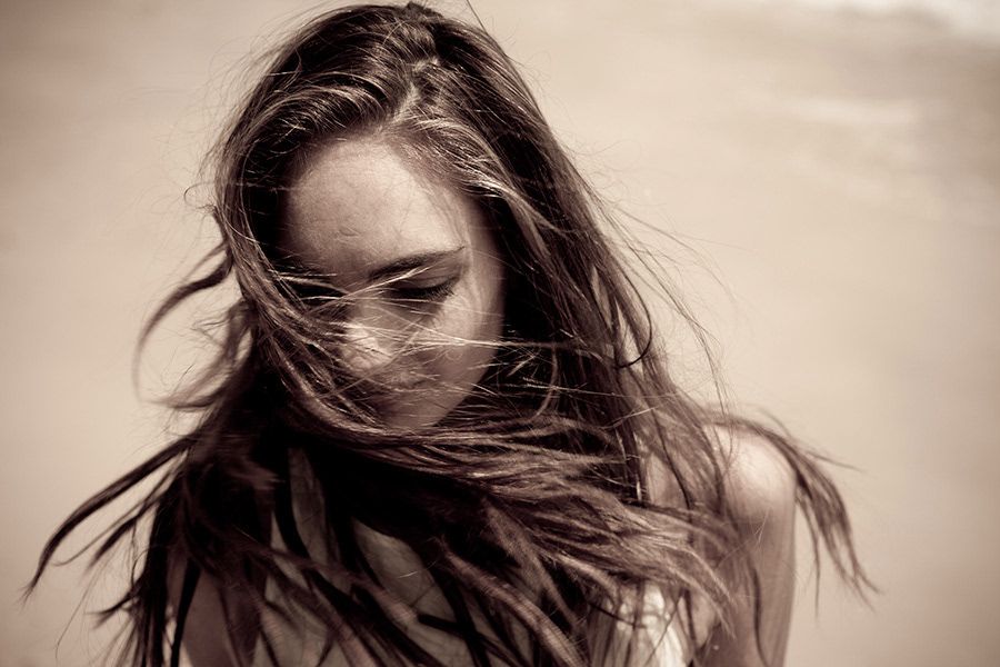Sepia-toned portrait of a woman with long dark windswept hair blowing across her face outdoors.