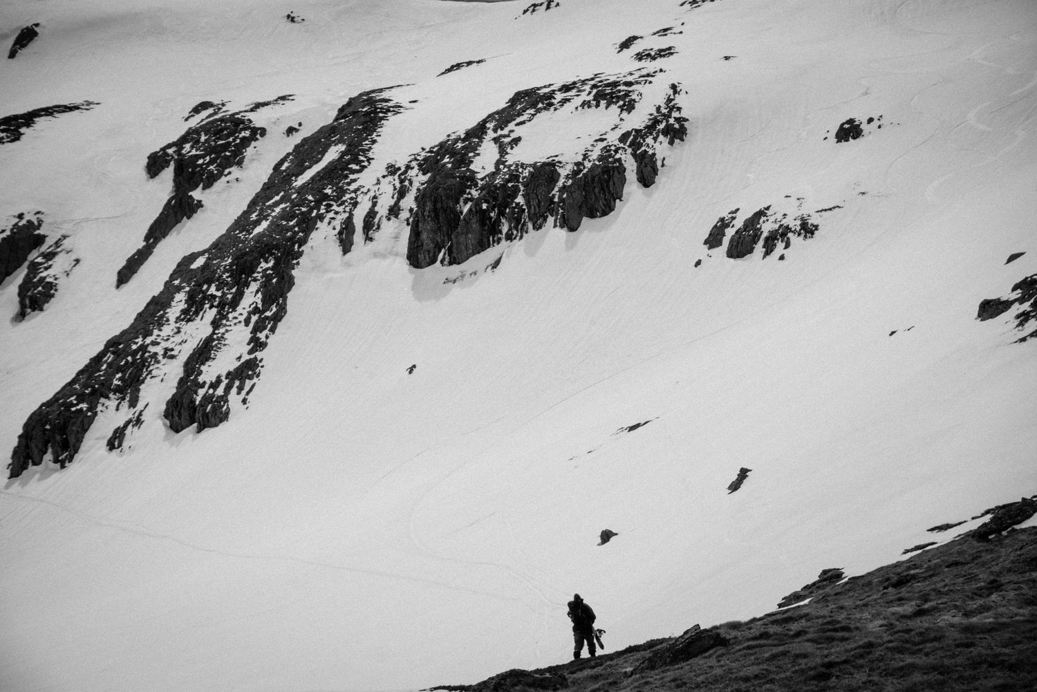 Lone hiker trekking across a vast snow-covered mountain landscape in black and white.