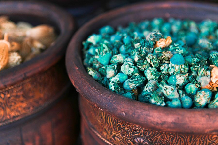 Turquoise gemstones displayed in ornate carved wooden bowls at a traditional market stall.