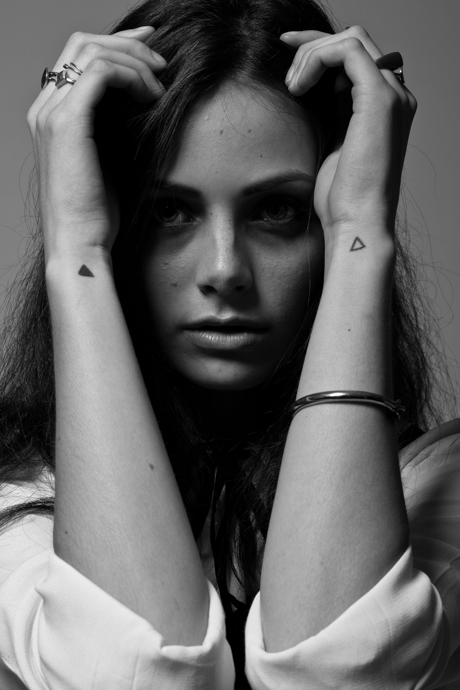 Black and white portrait of brunette woman with triangle tattoos on wrists.