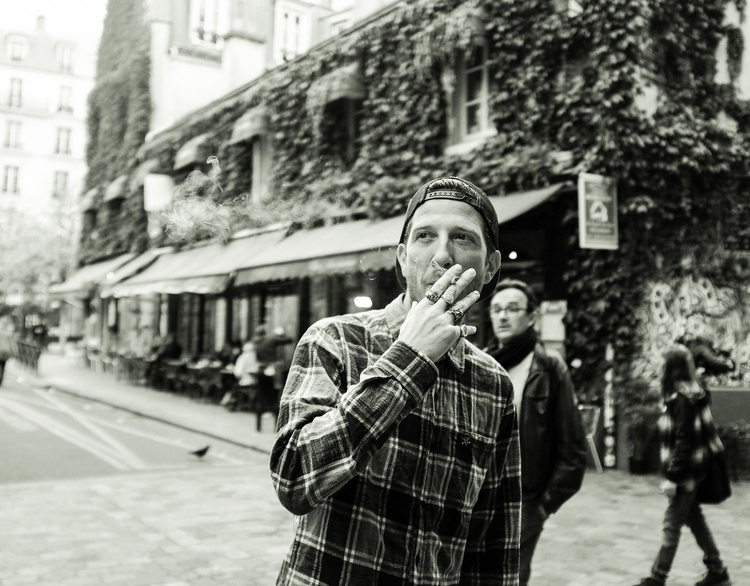 Black and white street photo of a man smoking outside an ivy-covered Parisian building.