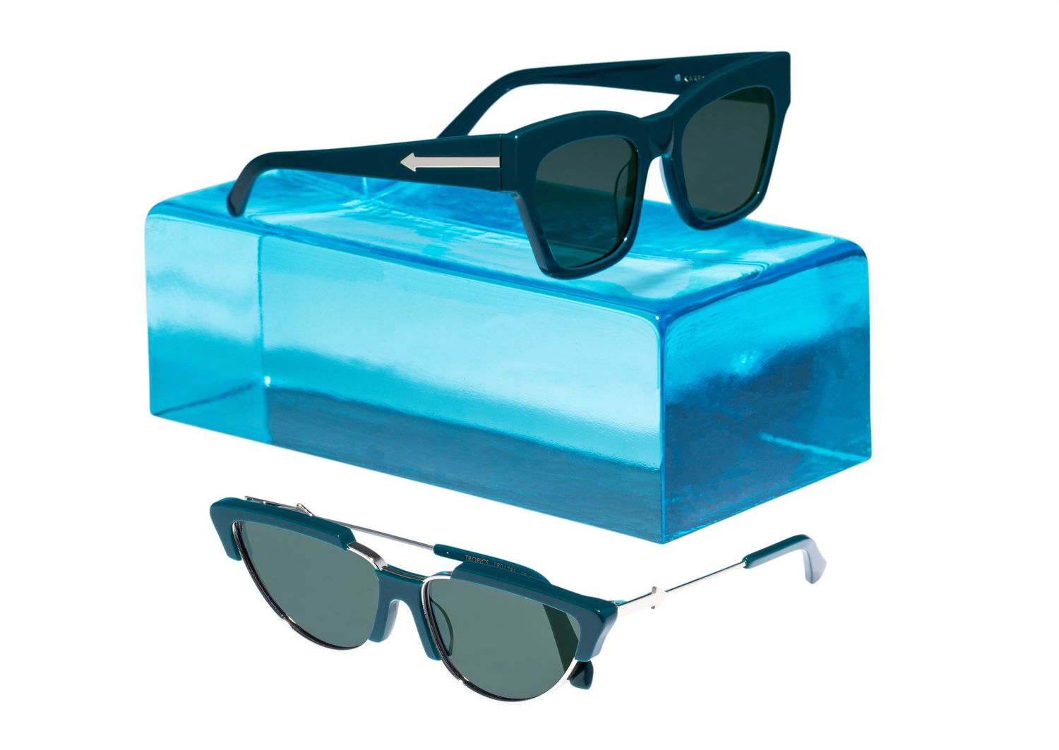 Two pairs of black sunglasses displayed on a translucent blue acrylic block prop.