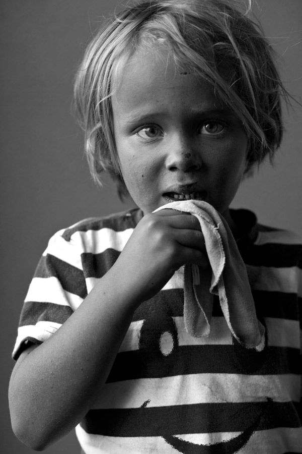 Black and white portrait of a young blonde child in a striped shirt holding a cloth to their mouth.