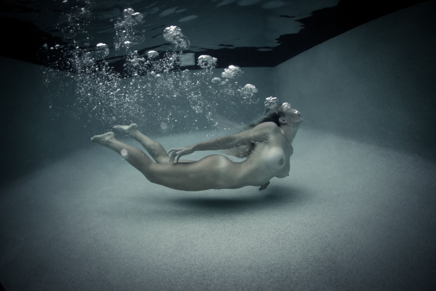Artistic underwater photograph of a nude woman floating gracefully with air bubbles.