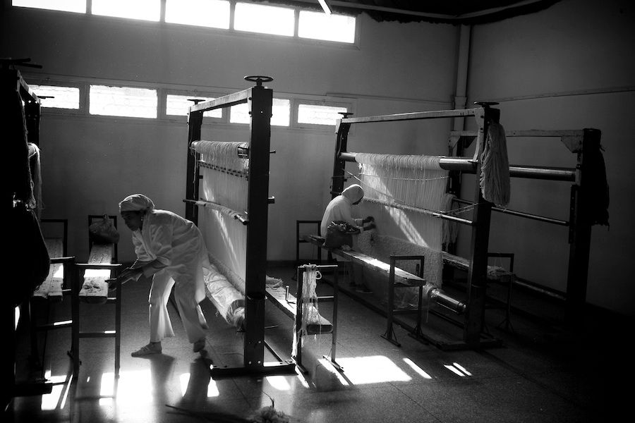 Black and white photo of workers operating traditional silk weaving looms in textile factory.