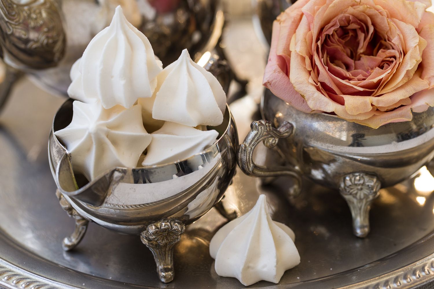 White meringue cookies in vintage silver bowl with pink rose on ornate silver tray.