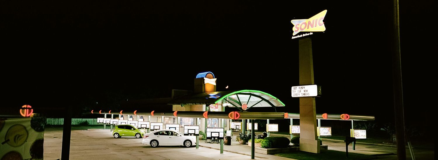 Panoramic night view of a retro American roadside motel and diner with neon signs glowing.