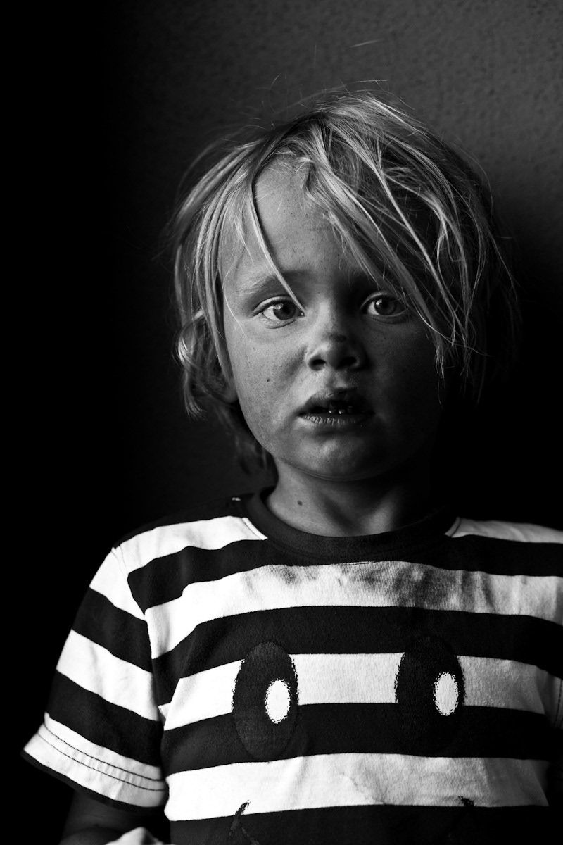 Black and white portrait of a young blonde child in a striped shirt looking up.