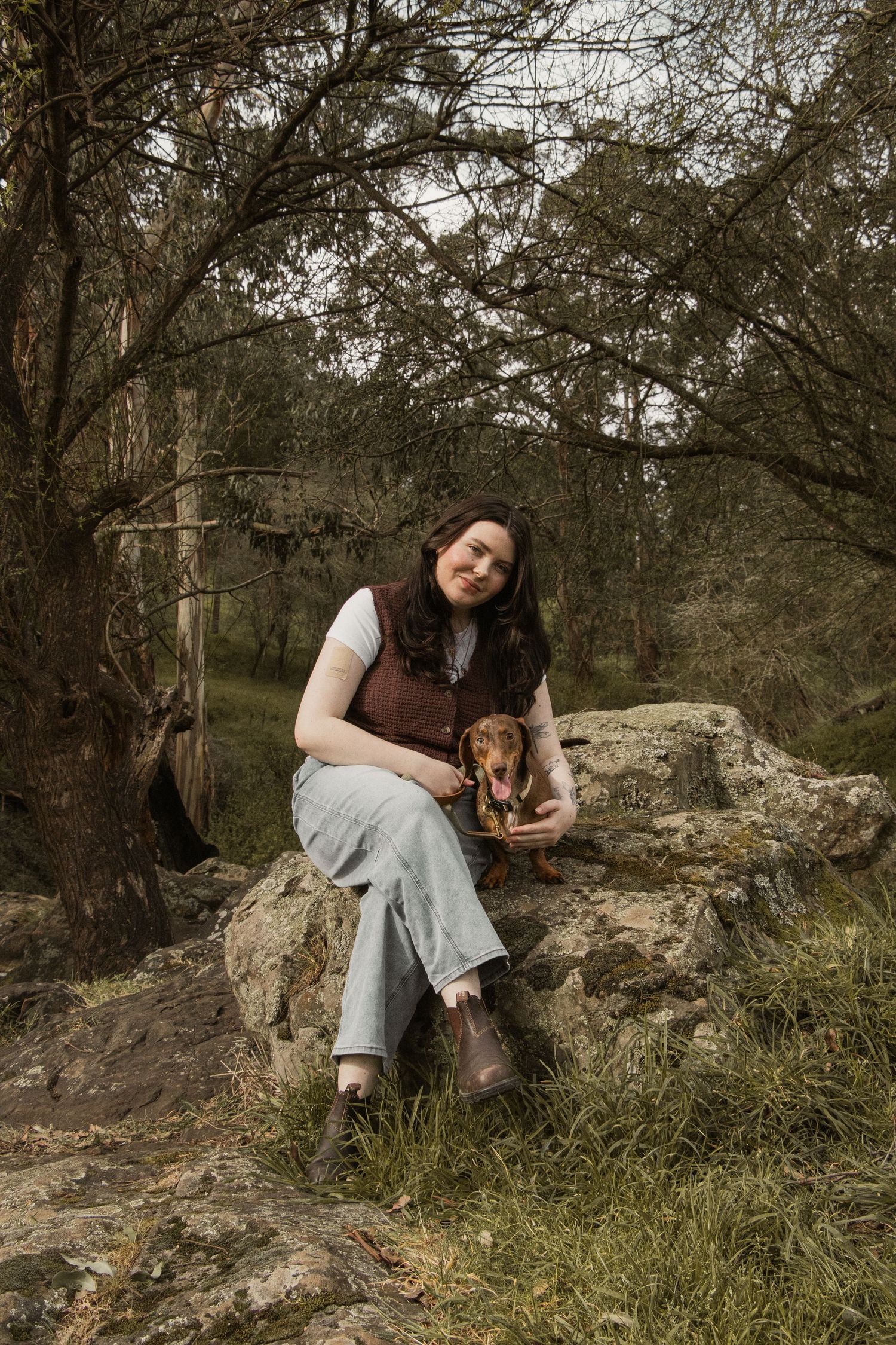 Pet owner and dog sitting together on a rock, in the afternoon during a pet photo session in the outdoors in Trafalgar, West Gippsland.