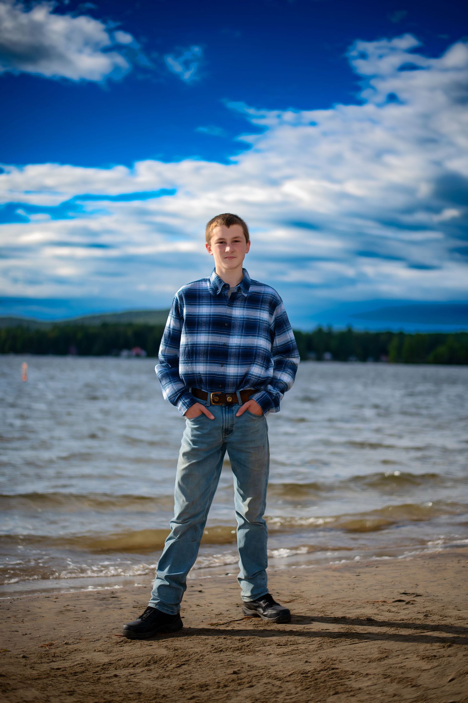 Person in plaid shirt standing on beach shoreline with dramatic cloudy sky.