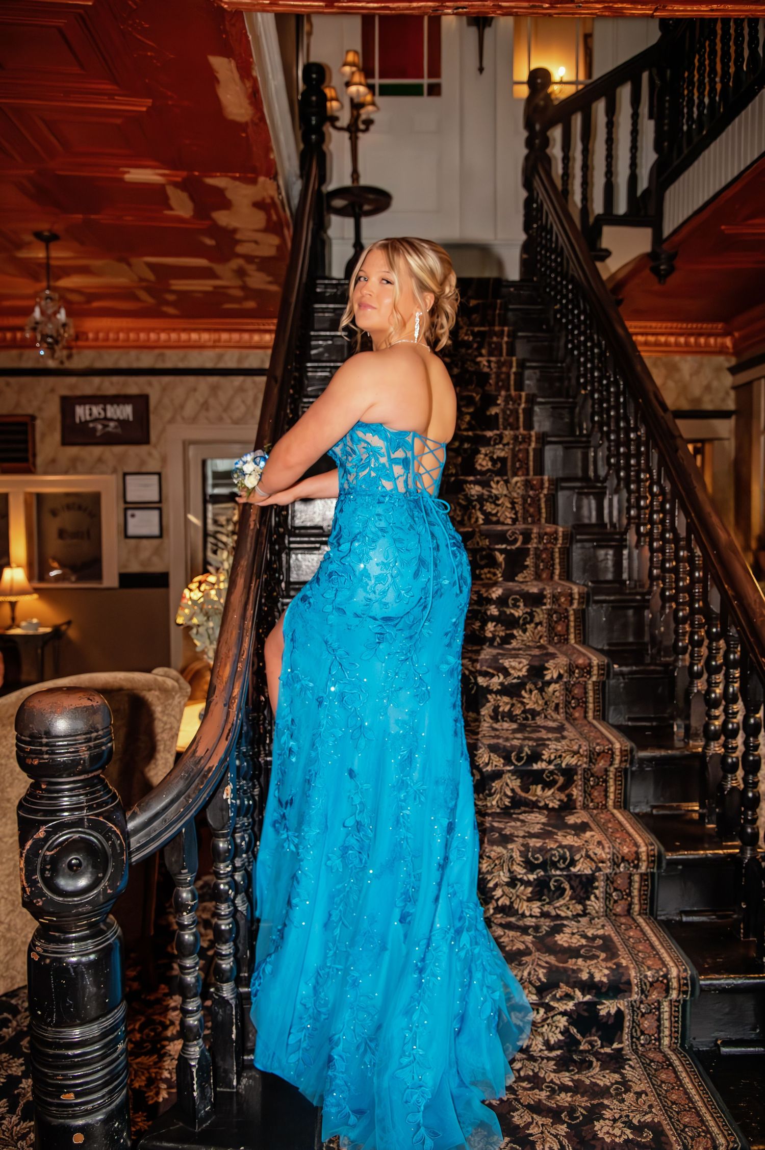 Flowing turquoise formal dress captured on historic staircase with dramatic lighting.