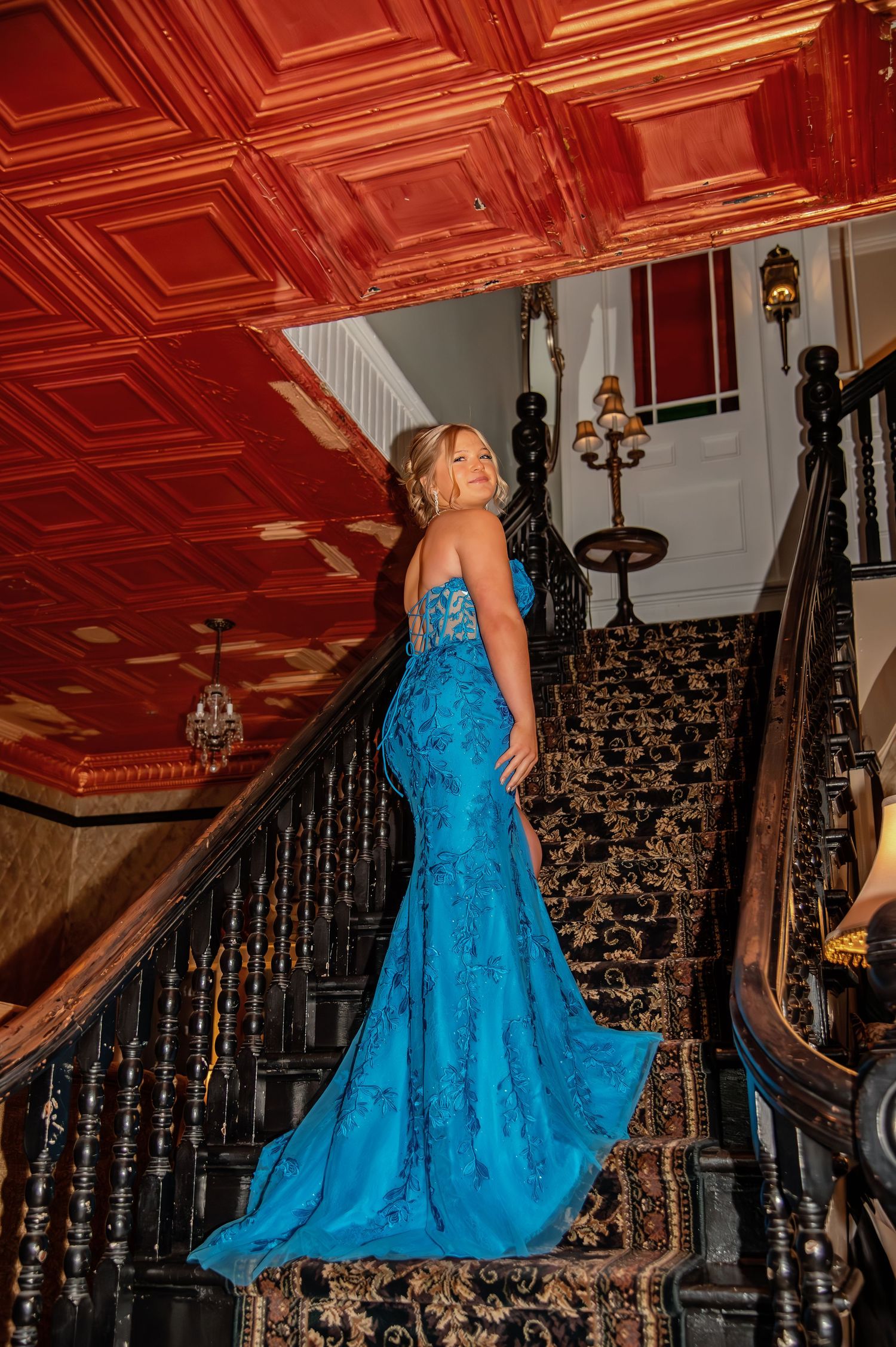 Elegant blue gown photographed against ornate staircase with warm copper ceiling details.