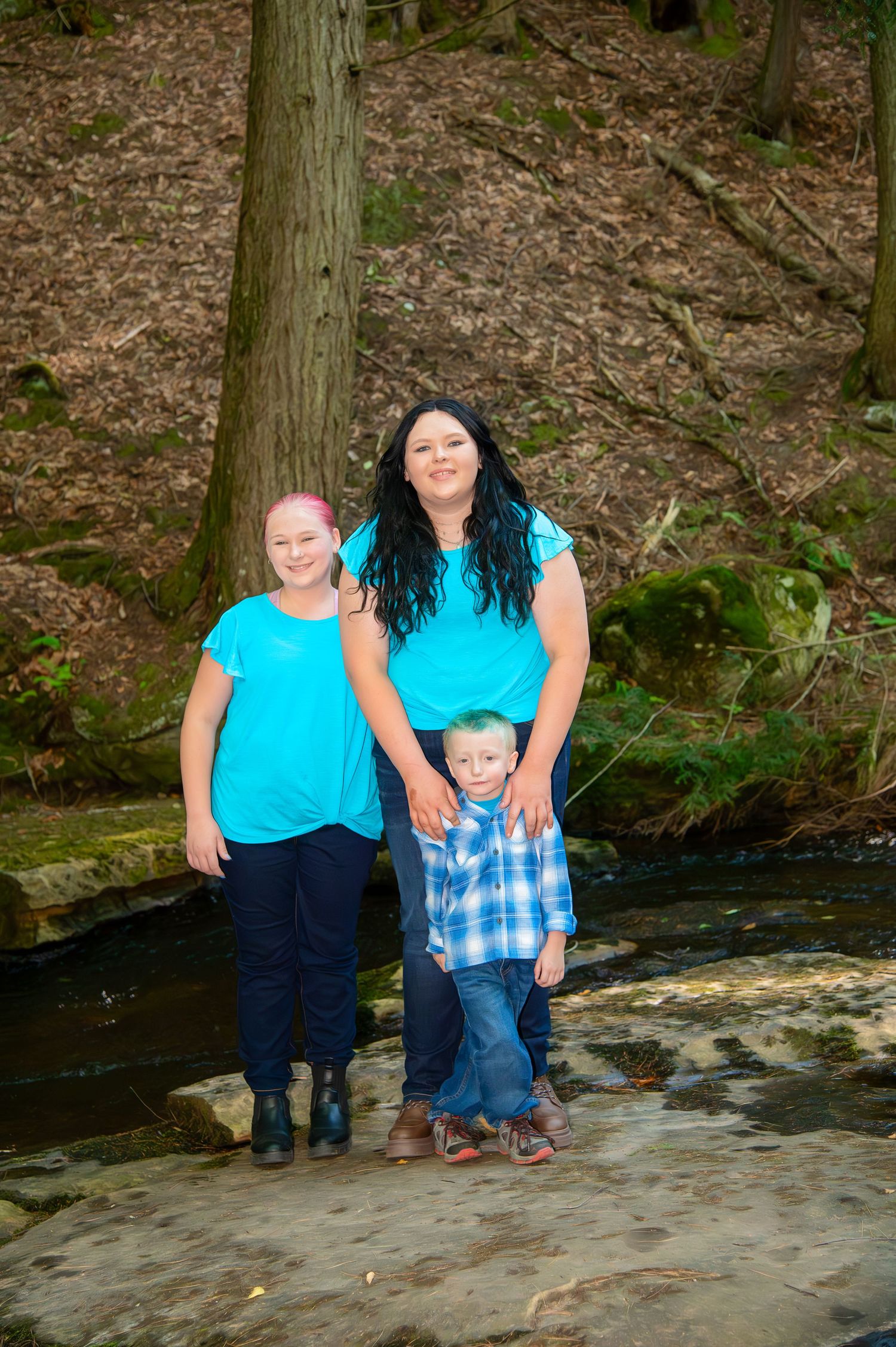 Family group poses together on rocky creek bed surrounded by forest.