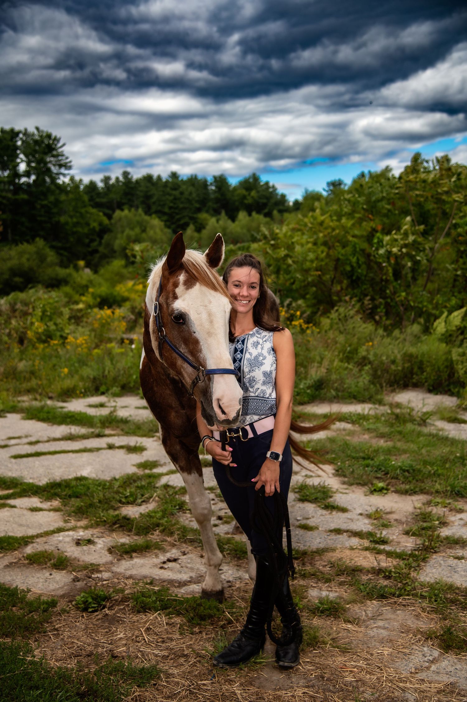 A paint horse stands with its companion on rocky terrain under dramatic storm clouds.