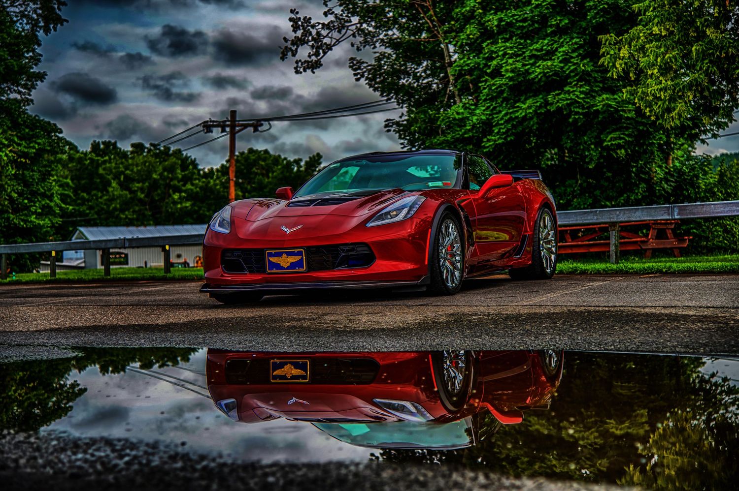 Red sports car parked under dramatic stormy sky with reflections.