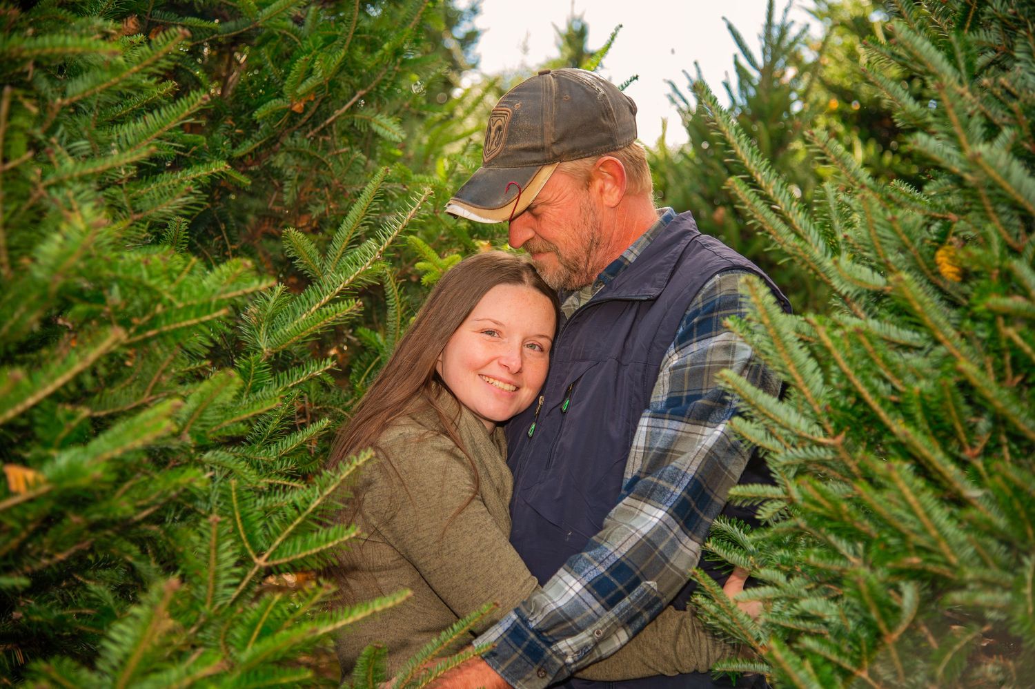 Couple sharing intimate moments among evergreen trees at a Christmas tree farm.