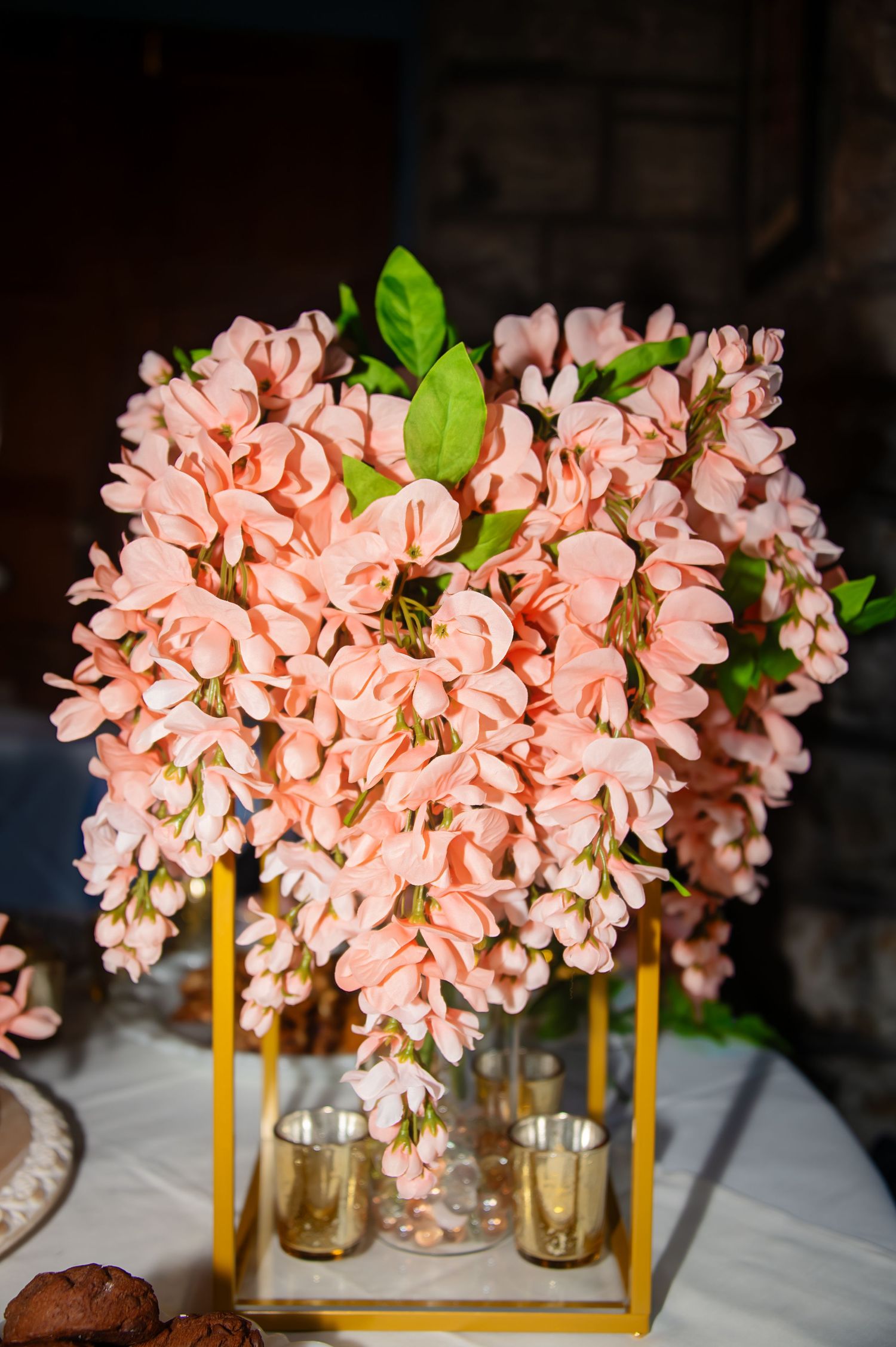 Elegant peach-colored floral arrangement in a gold geometric vase with decorative candle holders.