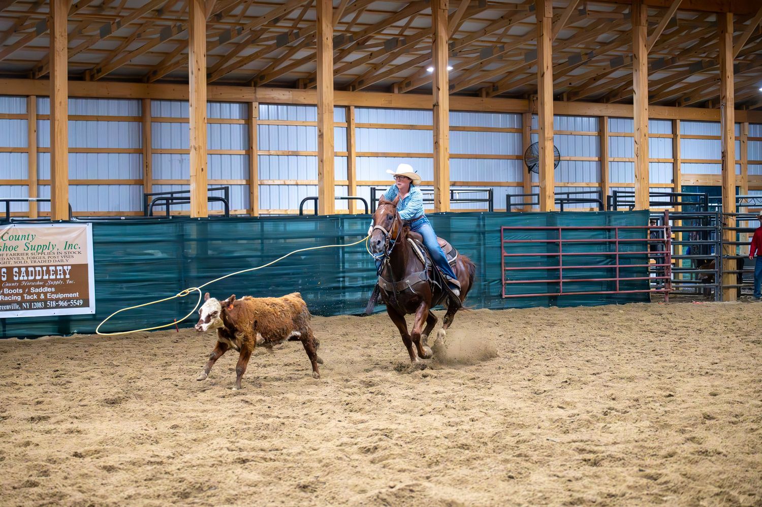 Panoramic view of rodeo competition in indoor arena with sponsor banners visible.