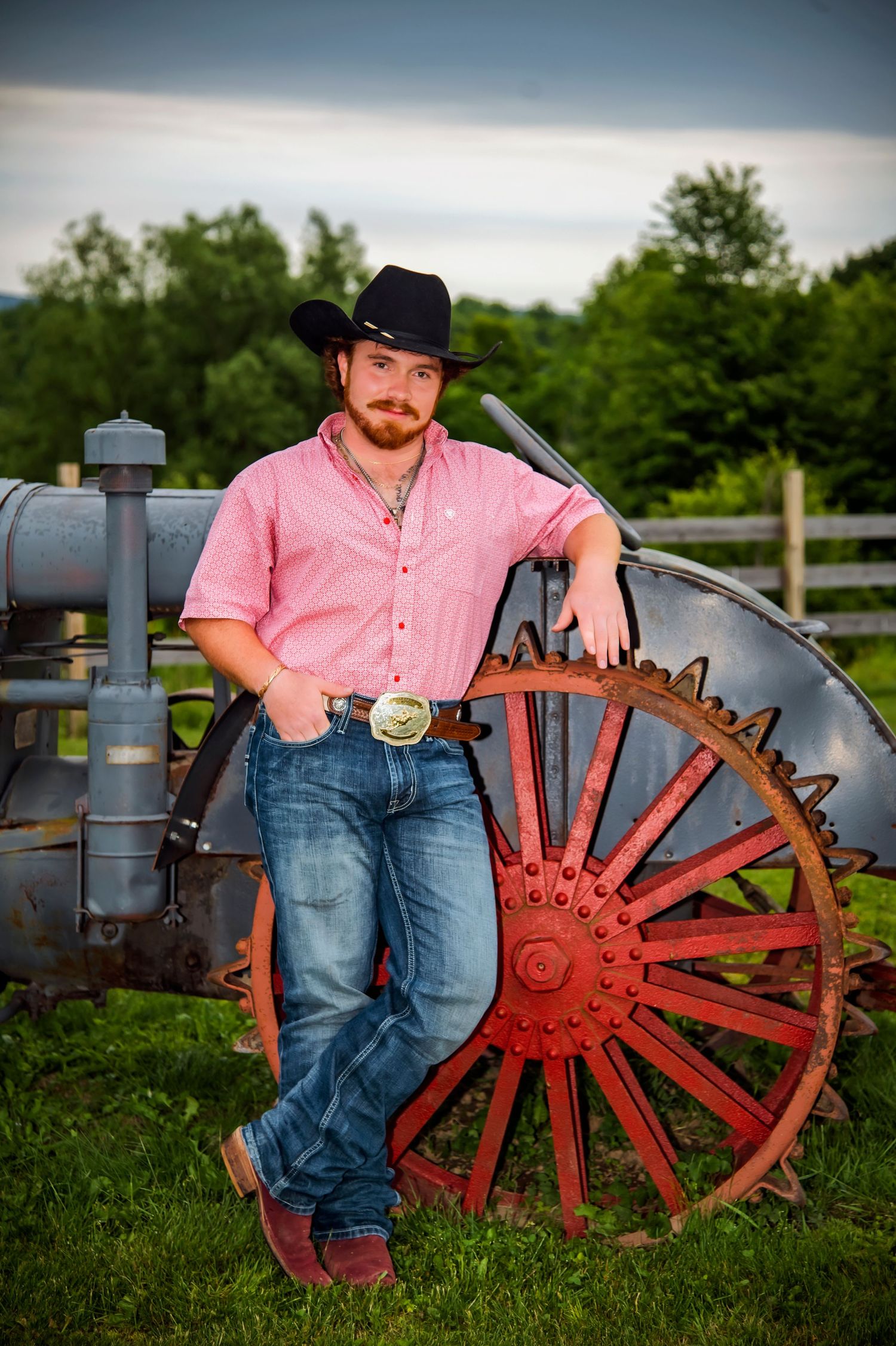 Country western style scene with antique wagon wheel and pink shirt against rural backdrop.