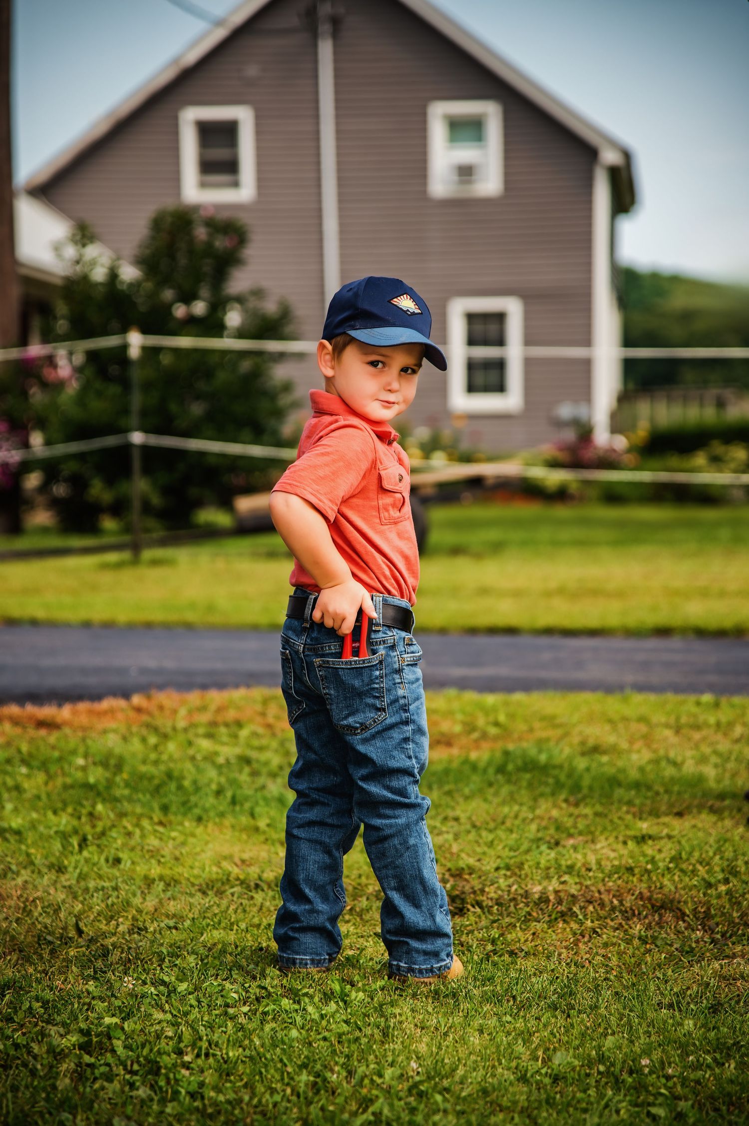 Small child in overalls and baseball cap playing in grassy yard.