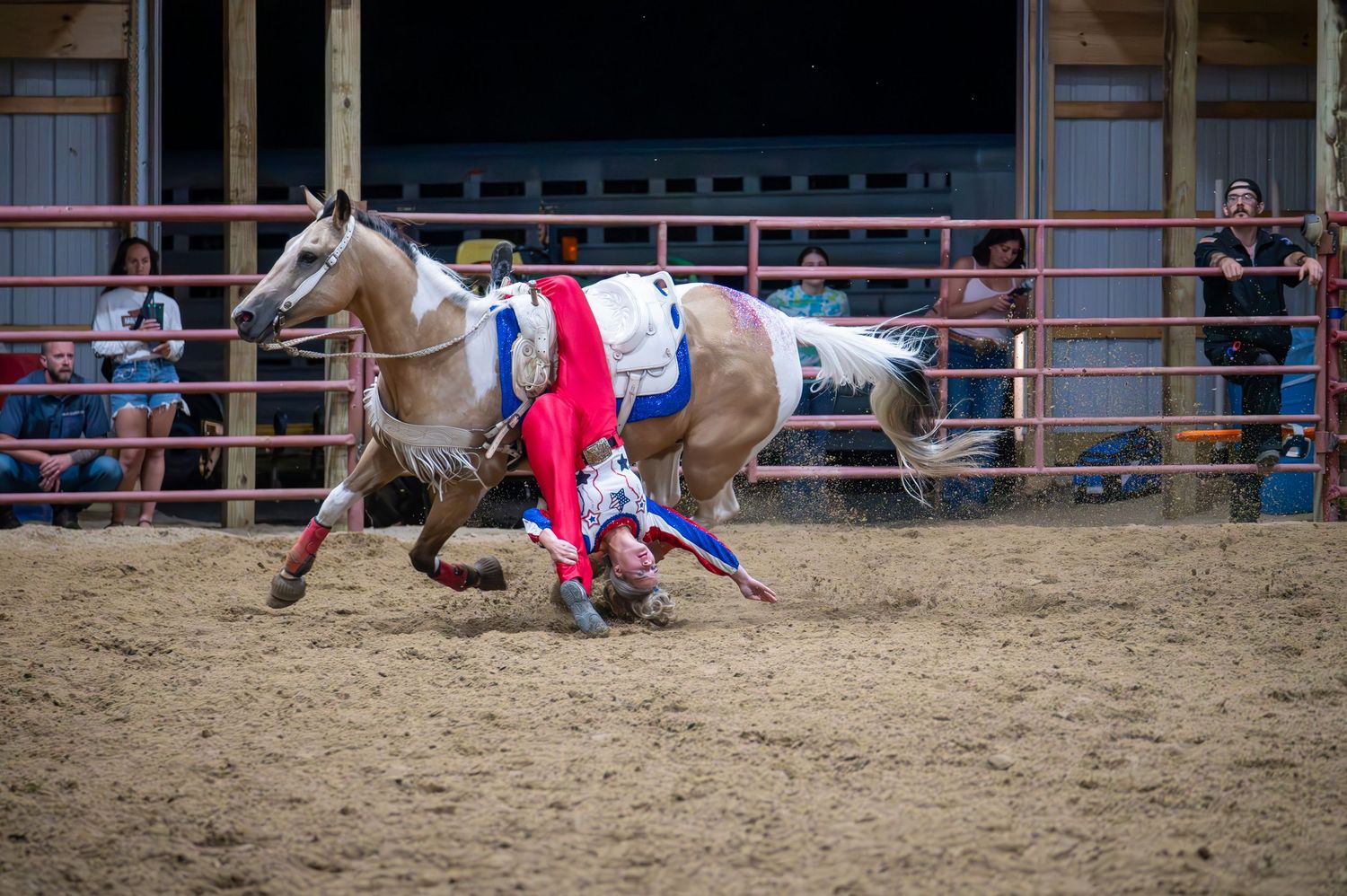 Rodeo competition with riders in red and blue uniforms performing in an indoor arena.