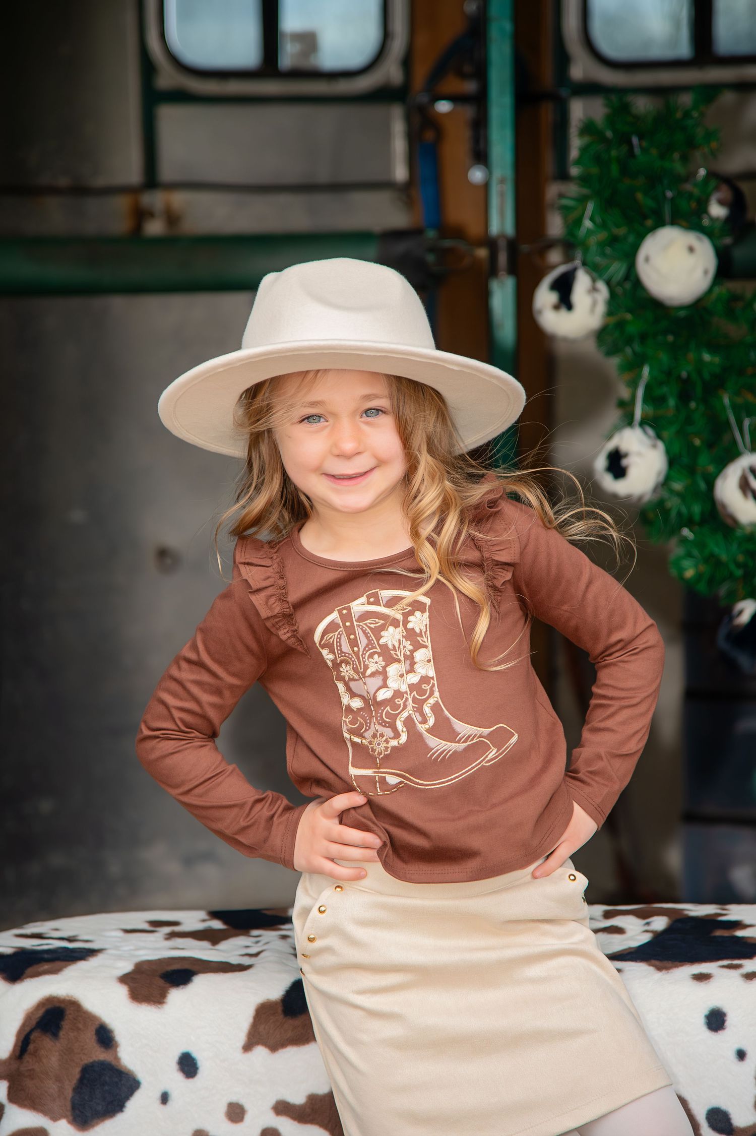 A brown dinosaur graphic t-shirt paired with cream colored pants creates a playful western outfit.