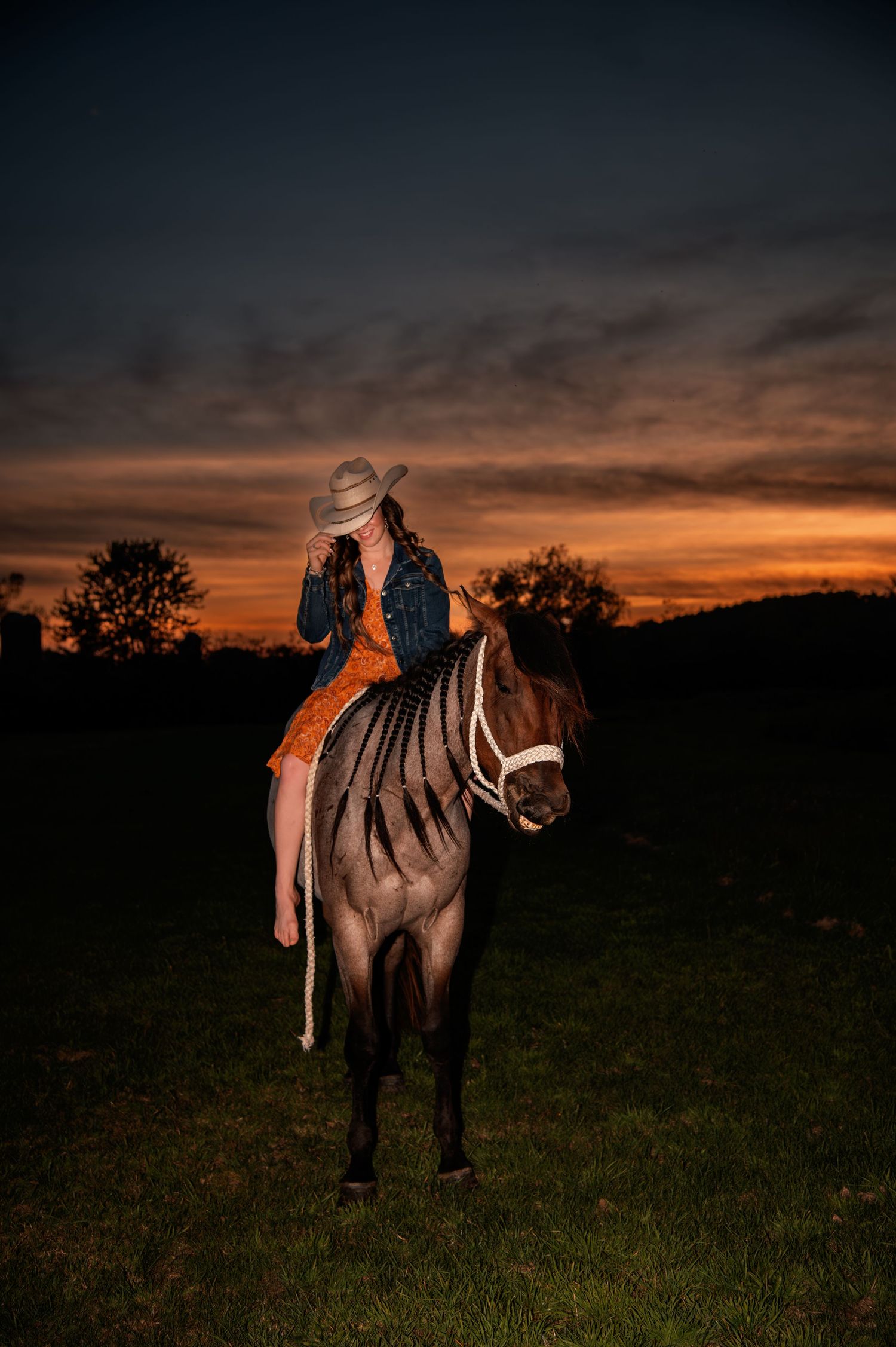 Silhouette of horse and rider against dramatic orange sunset sky.