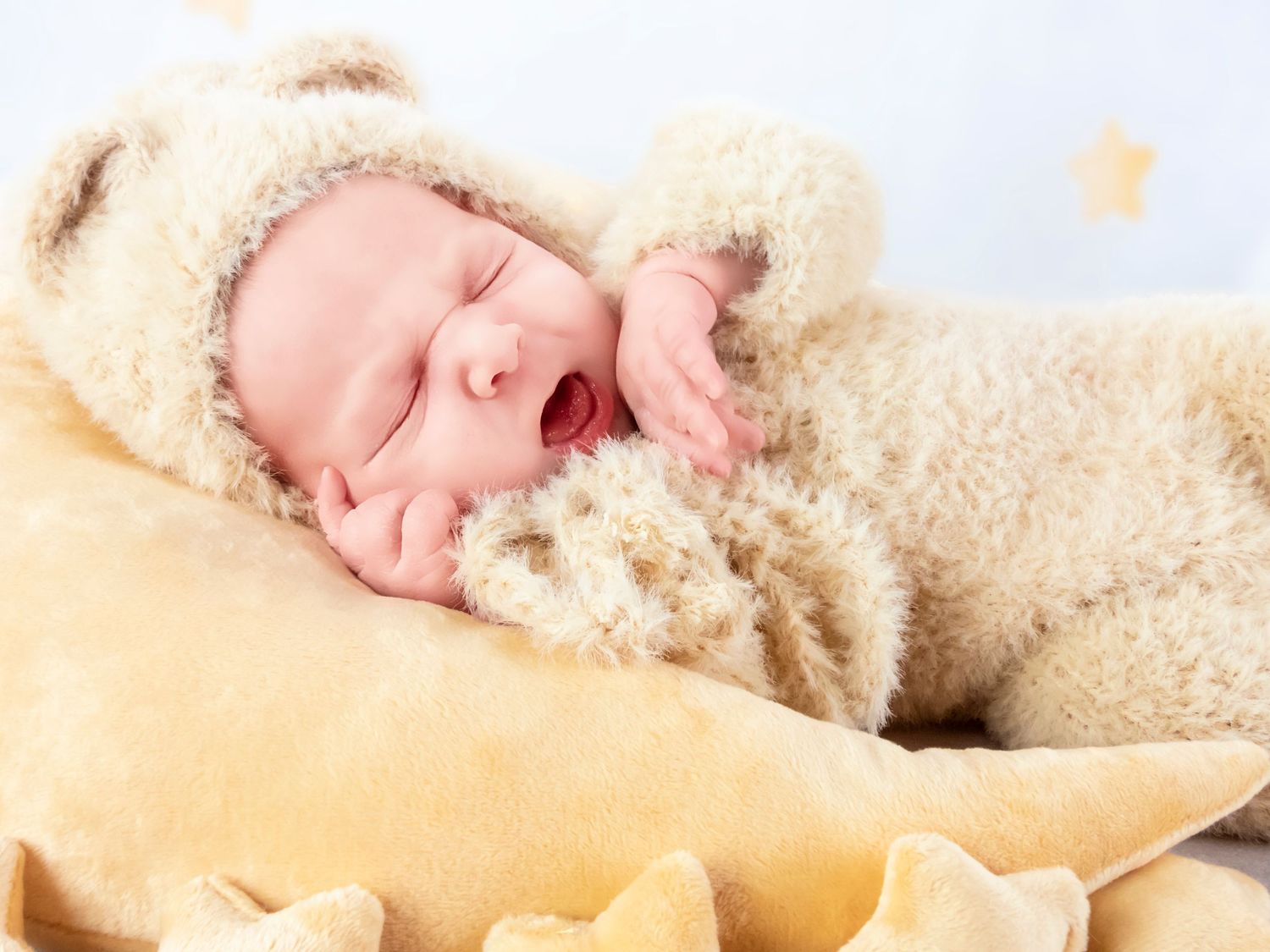 Sleeping newborn baby wrapped in cozy white blanket against cream background.