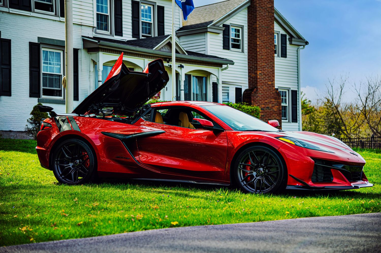 Red luxury sports car parked in front of white house with brick chimney.