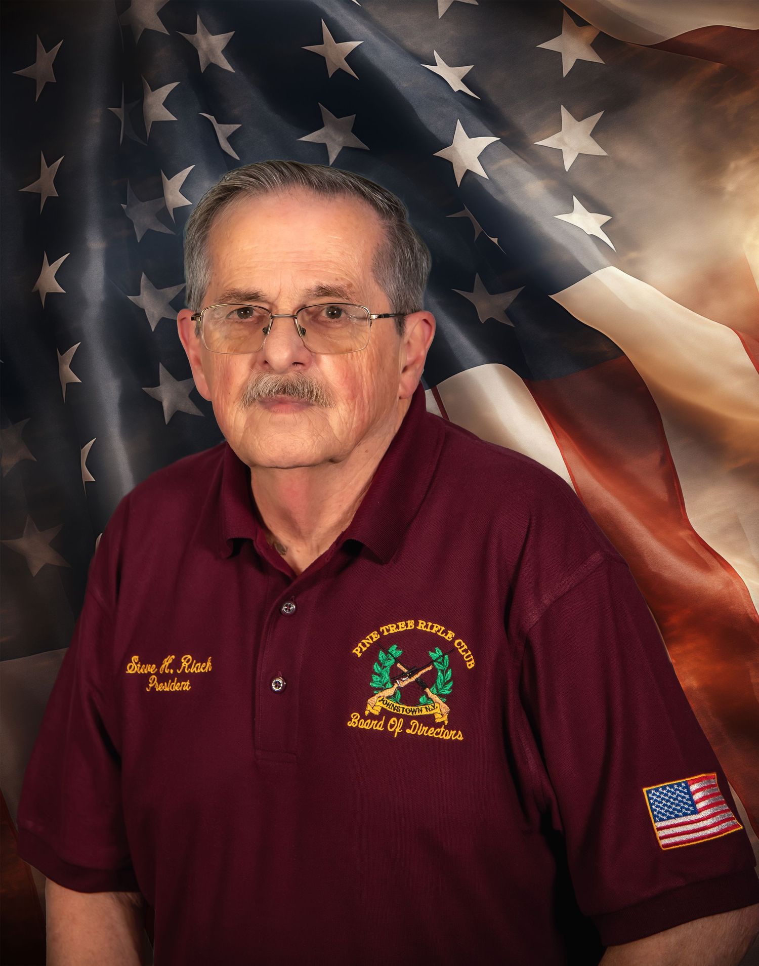 Veteran wearing burgundy polo with military patches poses against American flag background.