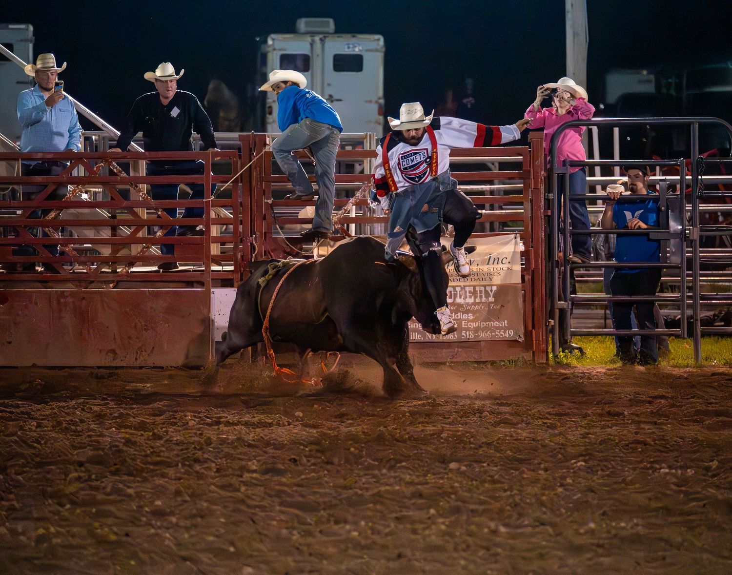 Nighttime rodeo action with riders competing in an illuminated arena.