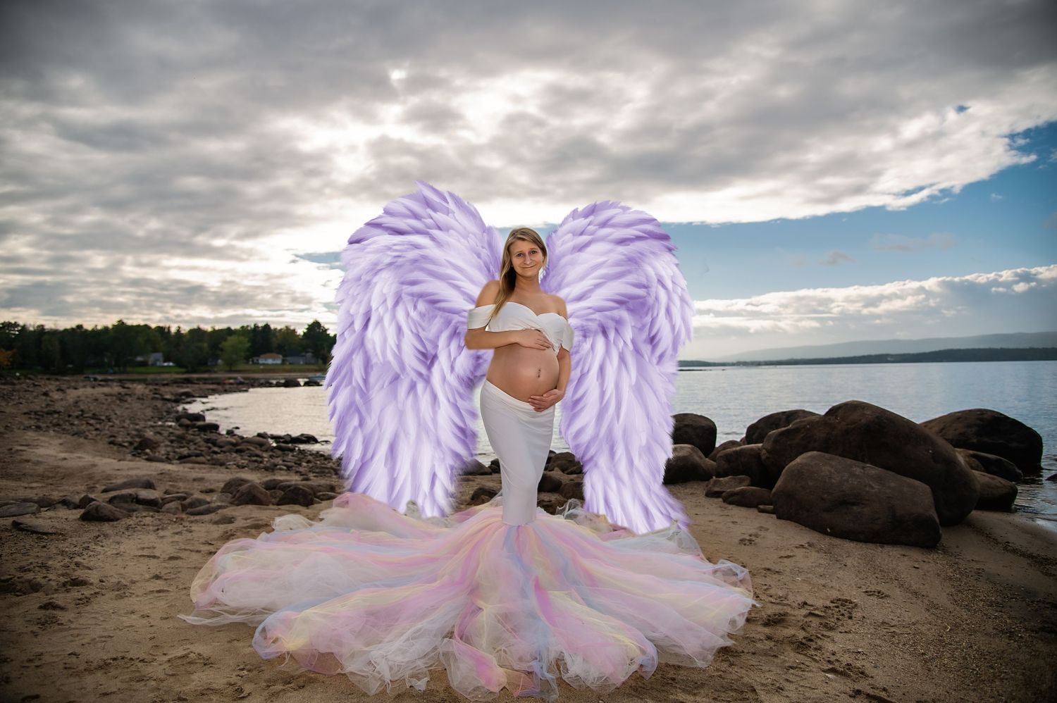 A person in a pink tulle dress and purple wings poses dramatically on a rocky beach at sunset.