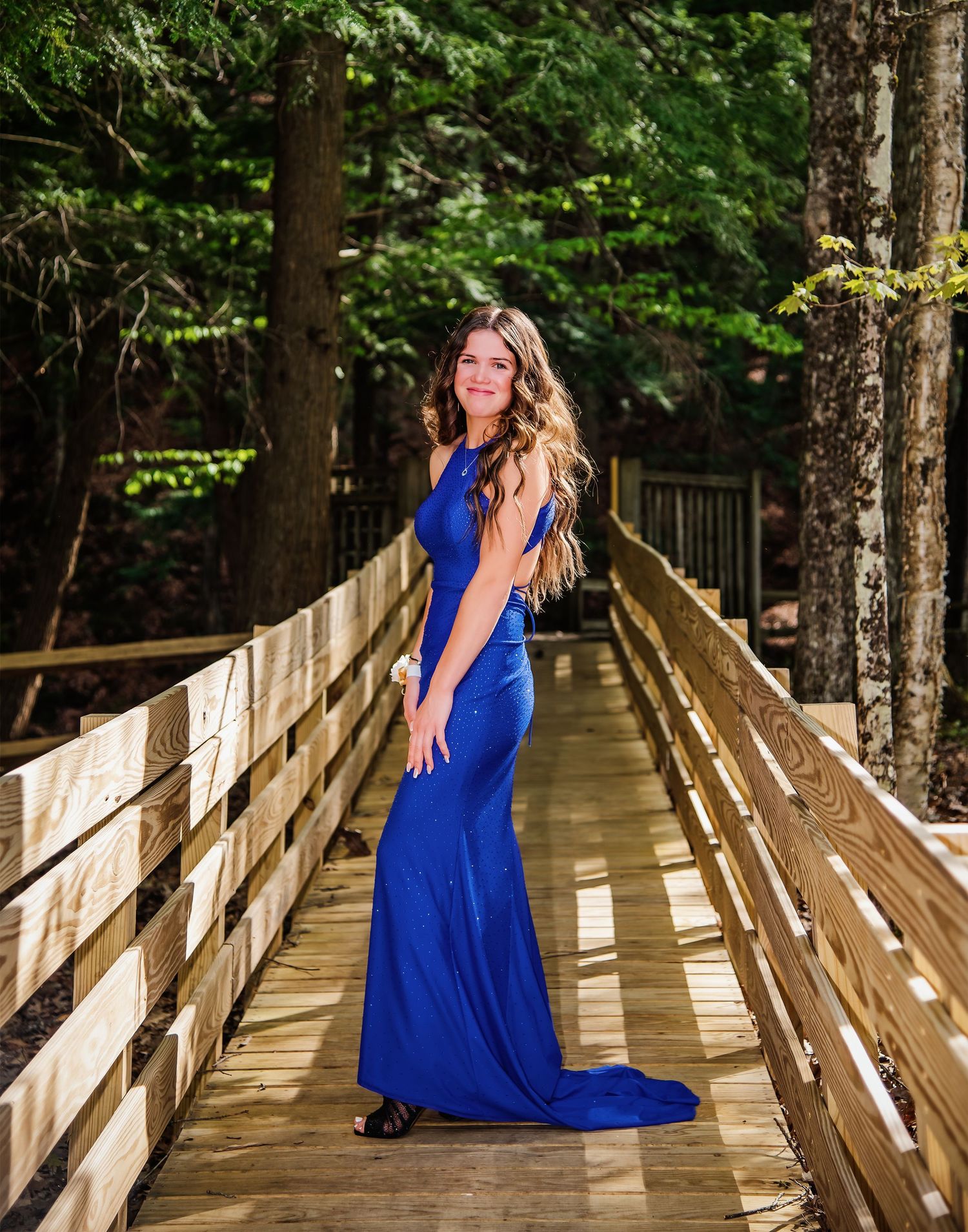 A vibrant blue dress flows elegantly on a wooden boardwalk surrounded by forest.